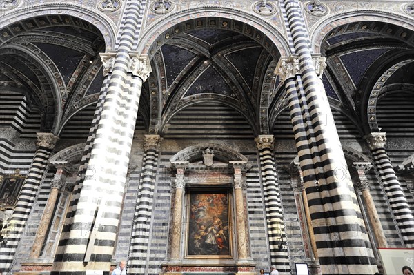 The nave of the cathedral with its black and white striped marble columns, cross and round arches,