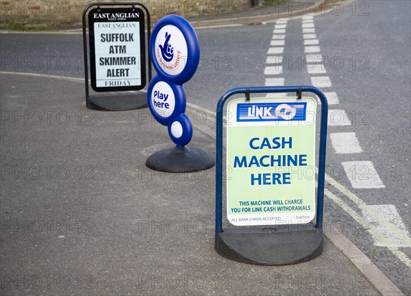 ATM sign outside shop with newspaper headline warning of scam taking place, Suffolk, England,