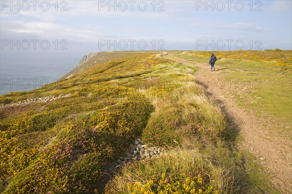 Woman wearing kagoule walking along the South West coast path at St Agnes head, Cornwall, England,
