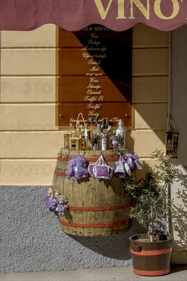 A wine barrel serves as a display area for bottles in front of a souvenir shop under warm sunlight,