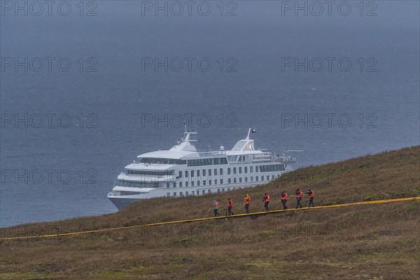 Passengers of the cruise ship Stella Australis in life jackets hike in storm and rain to Cape Horn,