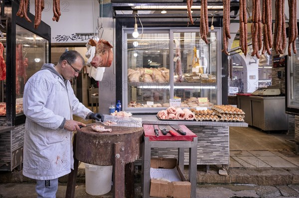 Butcher, meat trader cutting meat in front of his market stall, display of fresh meat, sausages,