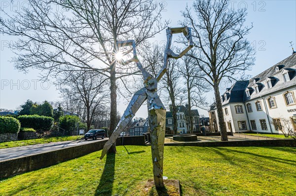 A modern metal sculpture in front of a castle, with the sun shining through its form, surrounded by