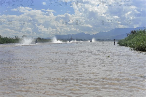 Speedboats create water fountains on a river with cloudy sky in the background, Inle Lake, Myanmar,