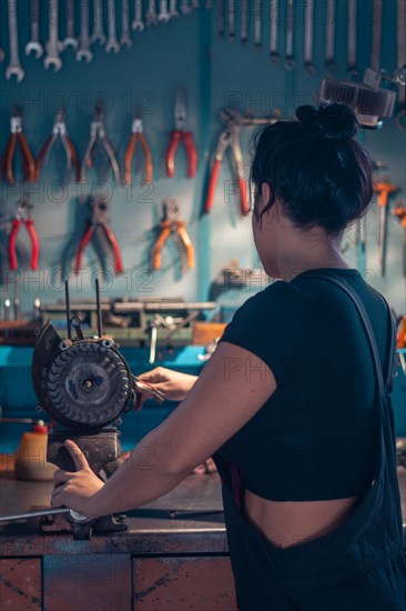 Female hispanic Mechanic working at a bench in a well-equipped workshop from behind, a complete