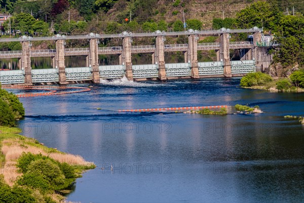 Landscape of dam releasing water through one floodgate into river with blue water located near