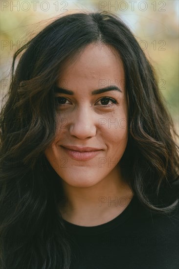 Serene outdoor portrait of a Cheerful hispanic young woman with a slight smile, appearing