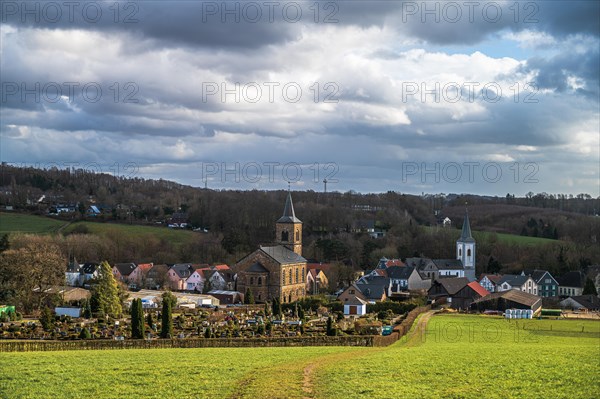 Picturesque view of a quiet village embedded in the green, rural landscape under a cloudy sky,