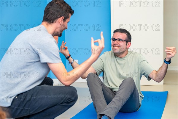 Yoga instructor helping a hand to a disabled man during a yoga pose sitting on the mat in the class