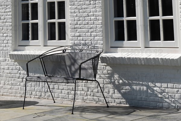 A black metal bench in front of a white wall casts a shadow in the sunlight