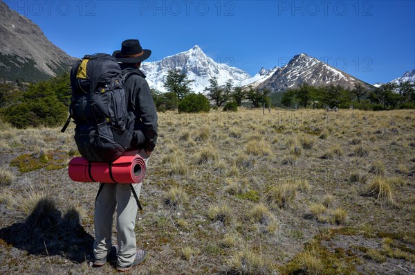 Hiker with a heavy rucksack in front of the snow-covered summit of Monte San Lorenzo, Perito Moreno