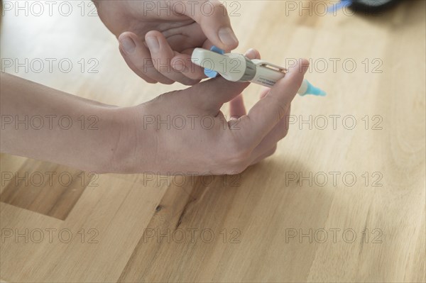 A lancet, lancing device, is held by a child in the right hand and drawn up to determine the blood