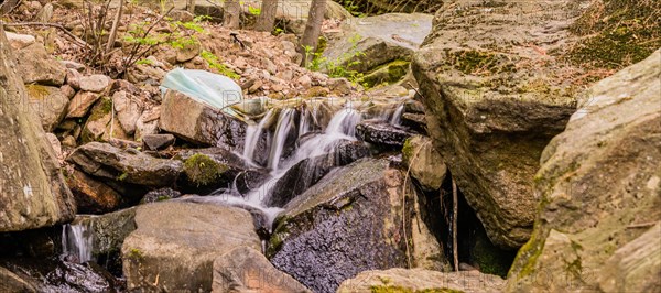 White plastic bag full of trash in stream of water cascading over large rocks and boulders in South