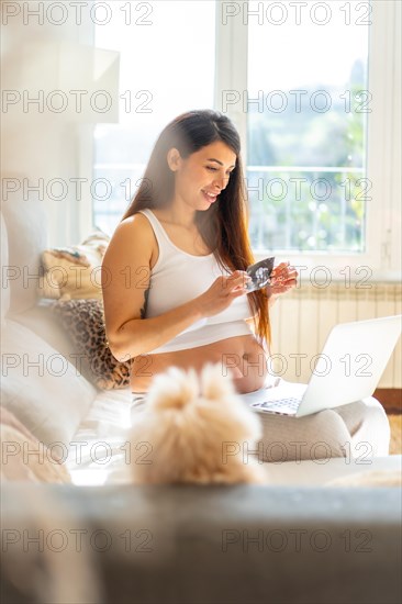 Vertical photo of a breauty adult pregnant woman showing baby ultrasound in video call using laptop