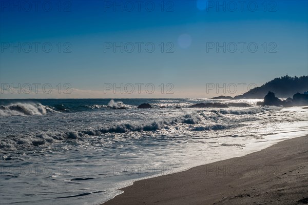 Rugged seascape with waves under bright morning sun crash onto beach and rocks under a beautiful