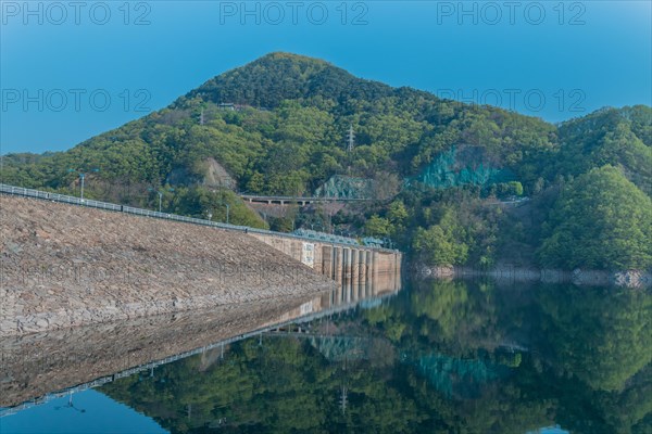 Beautiful lake area with dam and treeline reflected off the calm blue water at Daecheon Lake in