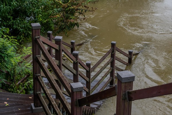 Wooden staircase leading to boardwalk submerged in river after torrential monsoon rains in Daejeon