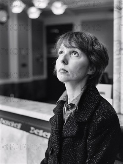 Black and white image of a contemplative woman gazing upwards, standing by a marble counter