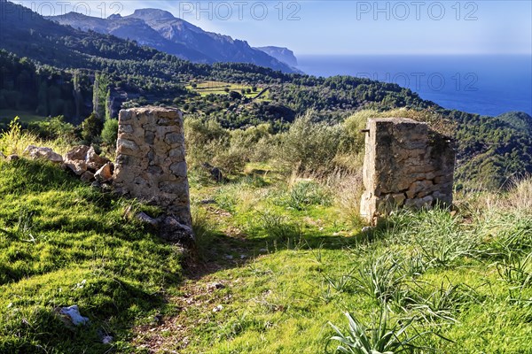 Stone pillars frame a rural scene with green fields and distant mountains, Hiking tour from