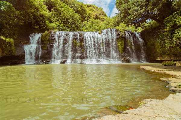 Landscape of a waterfall with trees and blue sky in the background and water basin in the