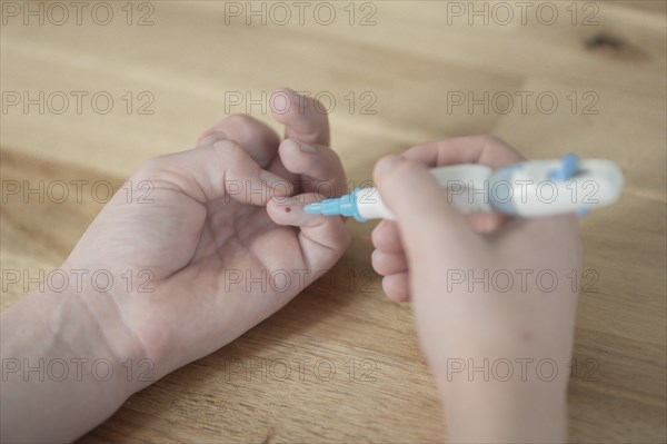 On the left a child's hand with a drop of blood on the little finger, in the right hand the child