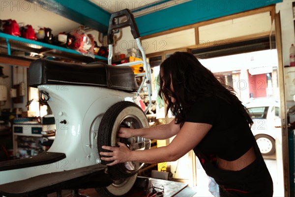 Hispanic young sensual long haired brunette woman Mechanic adjusting a tire on a vintage italian