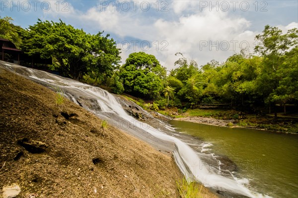 Side view of a waterfall cascading down a cliff into the basin below with green trees and blue,