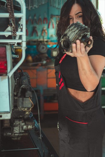 Professional latino female motorbike mechanic holding component of italianvintage scooter in a