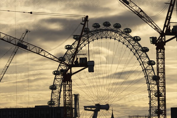 London Eye or Millennium Wheel tourist observation wheel at sunsetwith industrial cranes and