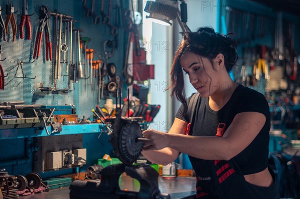 Serious young mechanic concentrating on repairing a scooter engine part in a vise in a well-lit