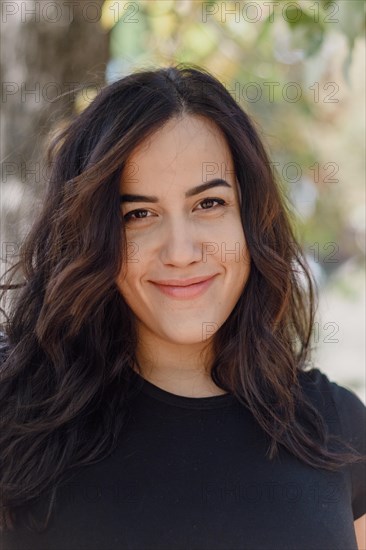 Outdoor image of a confident Cheerful hispanic young woman smiling in a black shirt with a relaxed
