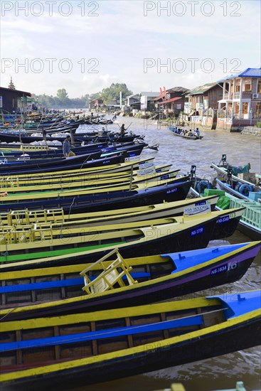 Row of colourful boats on a river bank with houses in the background, Pindaya, Inle Lake, Myanmar,