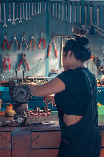 Woman mechanic repairing an alternator at a workbench in an auto moto workshop, wearing black