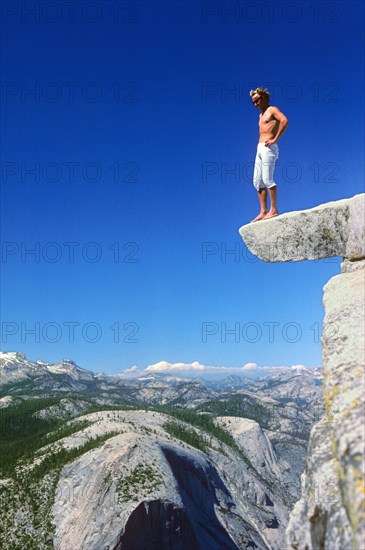 A man makes a test of courage and stands on a ledge at the top of Half Dome, 600 metres above the