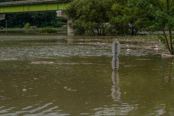 Round traffic signs and trees near bridge submerged in flooded river after torrential monsoon rains