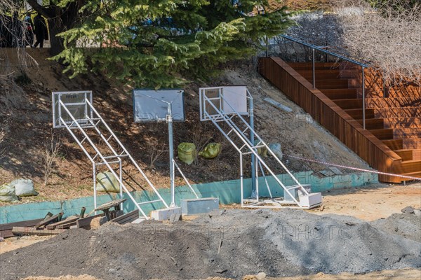 Construction equipment and a pile of earth sit near wooden stairs under a bright sun, in South