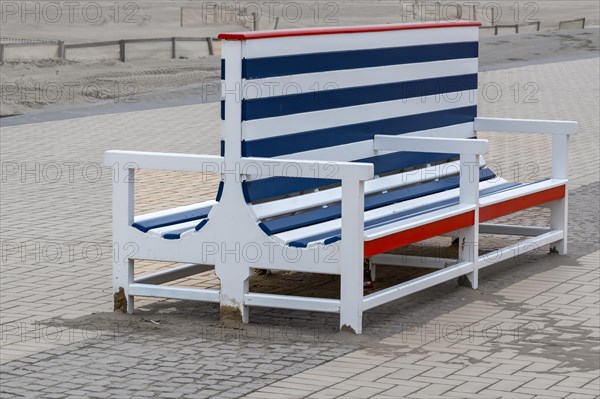 A large, empty beach chair with red, blue and white stripes stands on a cobbled path, Zeebrugge,