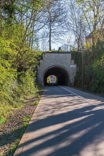 Sunlit tunnel at the end of an empty street surrounded by greenery, cycle path, Nordbahntrasse,