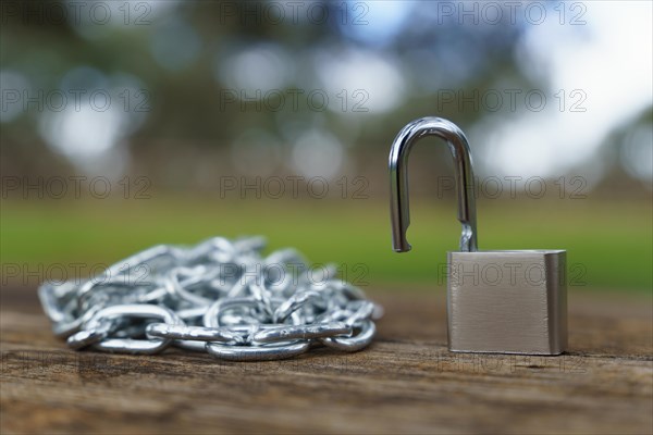 Close-up of an open padlock next to a chain strung on a wooden table in a field with an