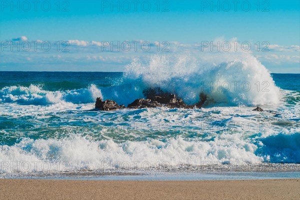 Dynamic white waves collide with coastal rocks on a sunny day with a vibrant blue ocean, in South