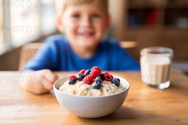 Table with bowl with healthy breakfast oatmeal porridge with berry fruits and happy smiling young