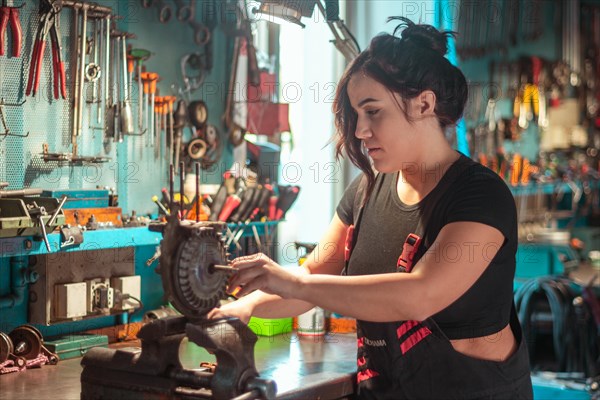 A woman is attentively working on a mechanical piece at a tidy workshop bench, a complete tool
