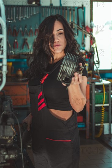 Hispanic Woman with mechanical part in hand, concentrating on her work in a workshop, a complete