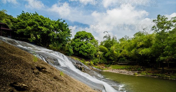 Side view of a waterfall cascading down a cliff into the basin below with green trees and blue,