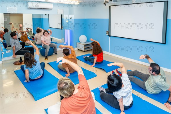 Elevated rear view of a group of male and female disabled people stretching during yoga class