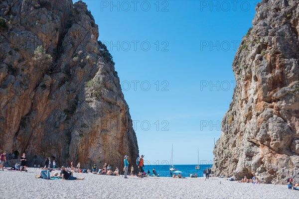 Torrent de Pareis, people relaxing on a popular tourist beach of pebbles framed by high cliffs,