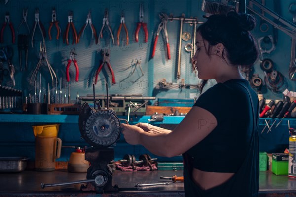 Mixed-race hispanic young Female mechanic, wear black overall, focused on an motorcycle part in a
