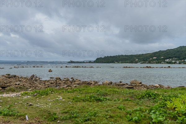 Seascape of rocky shoreline on a cloudy day with buildings on tree lined shore in the distance in