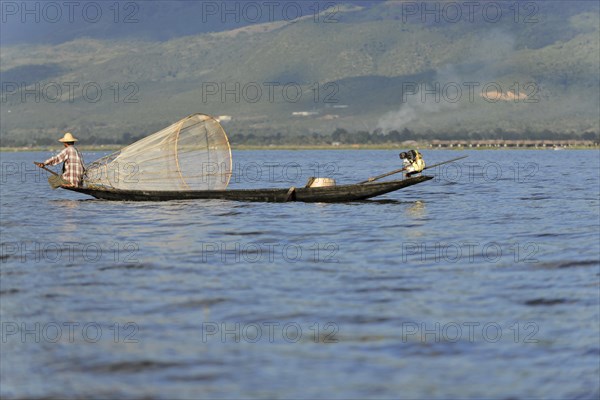 Fisherman enjoying the sun rays while working, surrounded by a mountain landscape, Inle Lake,