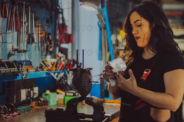 A female mechanic wearing overall in a workshop is carefully cleaning motorcycle parts, a complete
